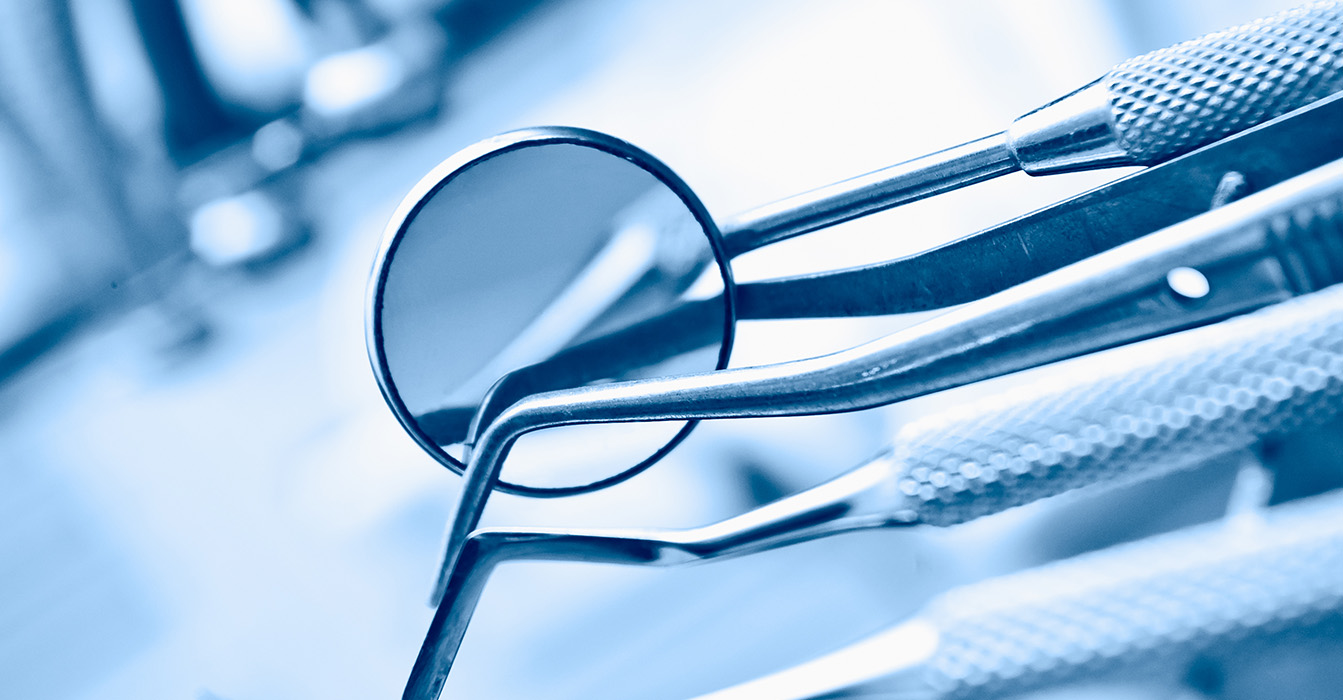 The image features a pair of eyeglasses with their lenses facing upwards, resting on top of a metal object, possibly a pair of tweezers or a similar tool, against a blurred background that suggests an indoor setting, likely a workshop or a laboratory.