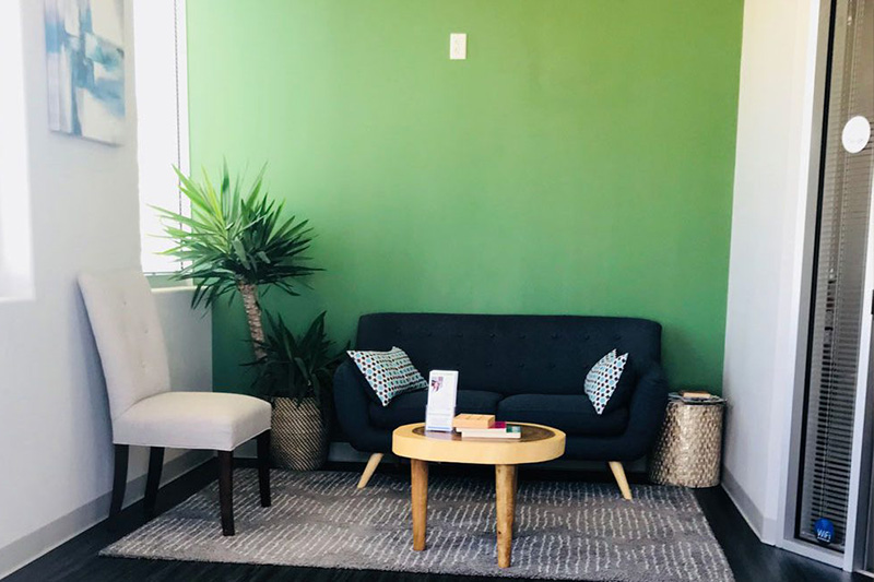 A room with green walls, a black sofa, a white chair, a coffee table, a potted plant, and a modern decorative style.
