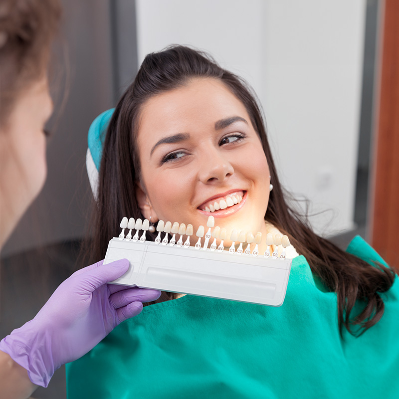 The image shows a woman sitting in a dental chair with her teeth being cleaned by a dental hygienist using an electric toothbrush.