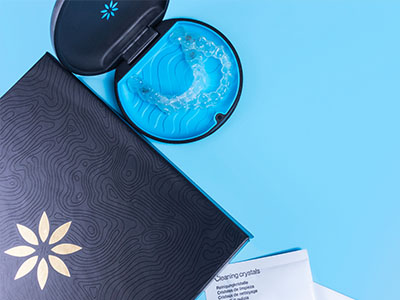 An open box with a blue object inside, placed on a surface next to a closed box with a similar design, against a light background.