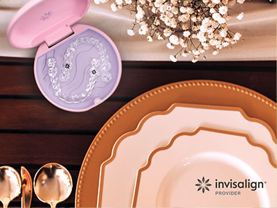 A photograph showing a dining table with various plates, a box of cosmetic product samples, and a purple lid with a design on top, against a backdrop of a wooden surface and decorative items.