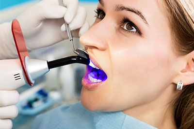 This is an image featuring a person receiving dental care with a dental drill in their mouth while wearing protective eyewear, being attended to by a dentist in a professional setting.
