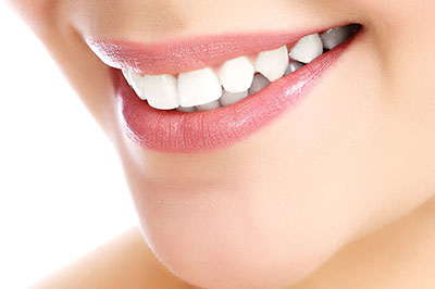 The image features a close-up view of a person s smiling face with white teeth and lips, emphasizing their dental hygiene, against a plain background.
