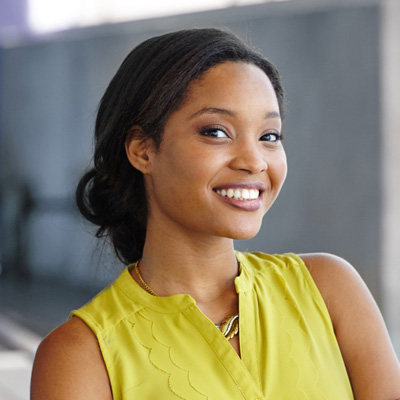 A woman with a bright smile wearing a yellow blouse poses for a portrait.