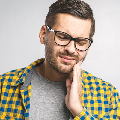 A man with glasses and a beard wearing a plaid shirt, looking downward with his hand on his chin, possibly expressing concern or contemplation.