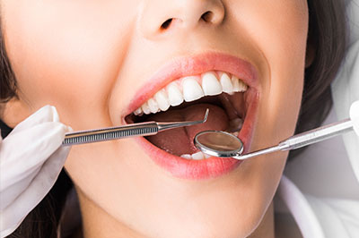 A woman receiving dental care with dental tools visible around her mouth.