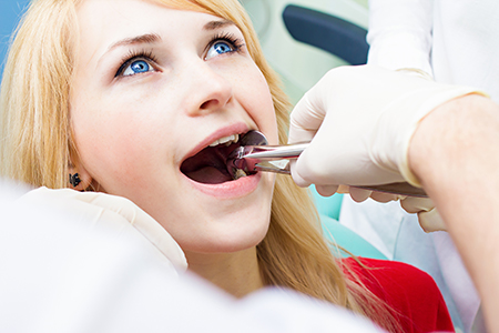 A woman receiving dental care, with a dentist using a drill on her teeth while she wears protective glasses.
