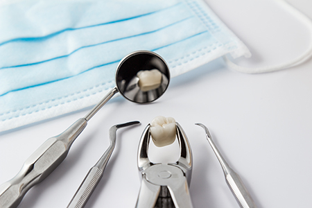 The image shows a collection of dental instruments, including tweezers and a dental drill, placed on a blue cloth with a medical mask nearby, suggesting a dental care setting.