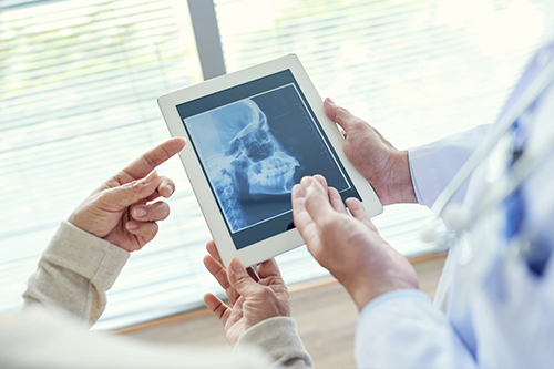 The image shows two individuals interacting with a tablet displaying an X-ray, with one person holding the device and another examining it, both appear to be in a medical setting.